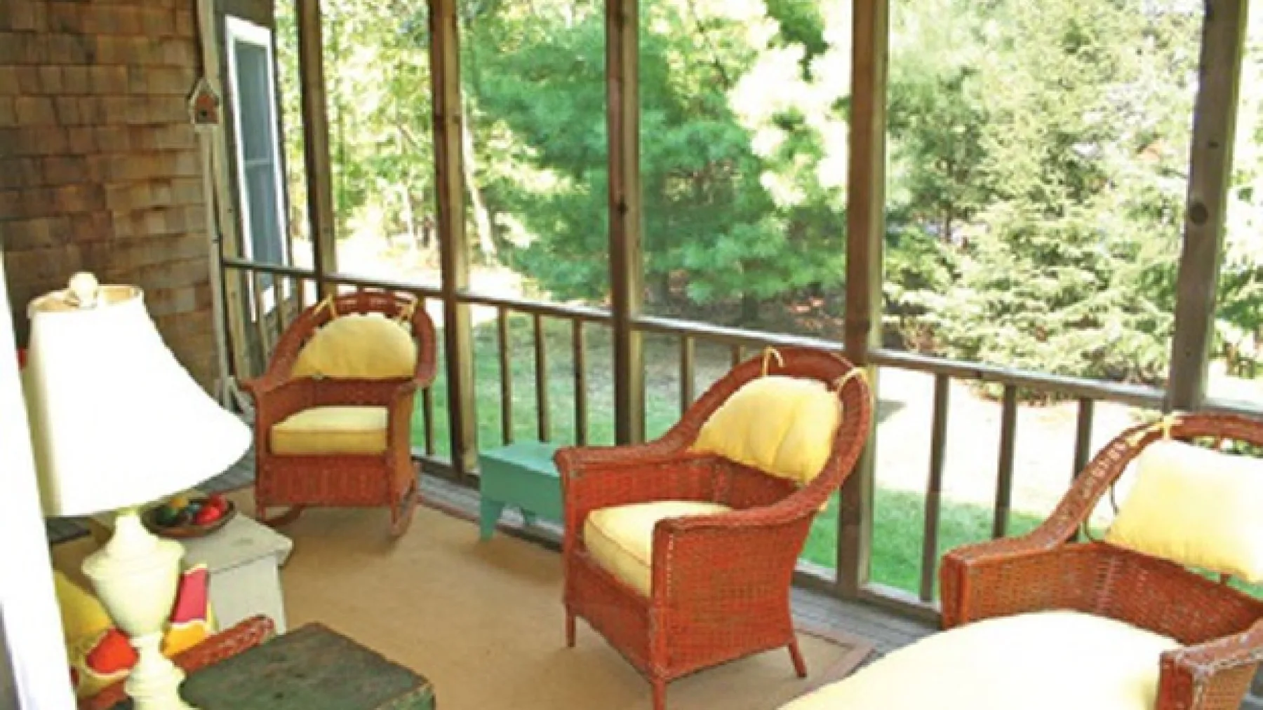 A sunroom with wicker seating and large windows overlooking trees.