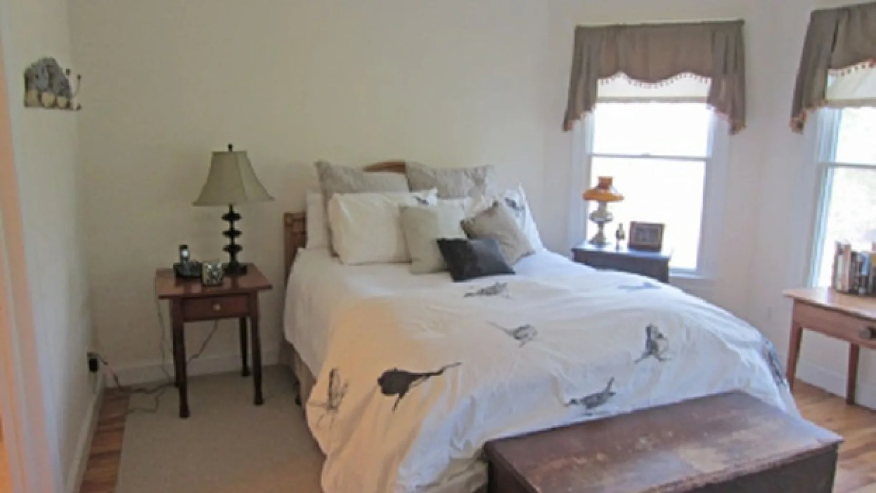 A bedroom with a large bed, white bedding, and windows.