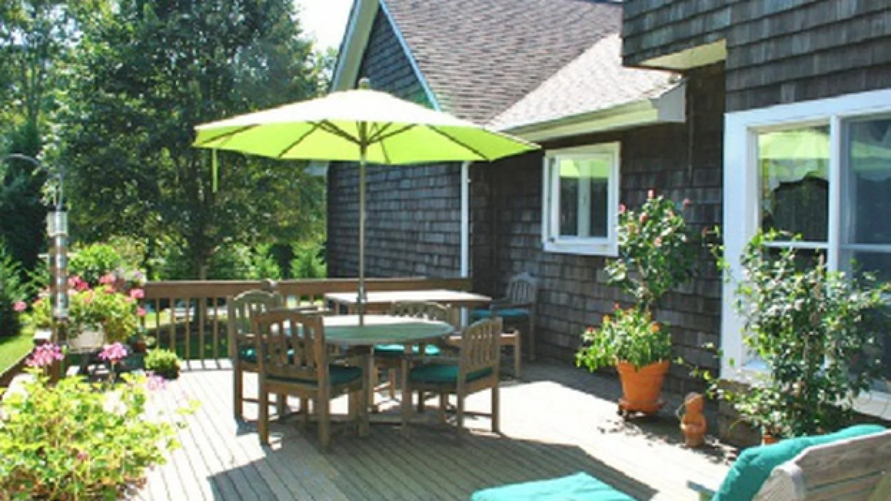 A sunny outdoor deck with a dining table beneath a green umbrella.