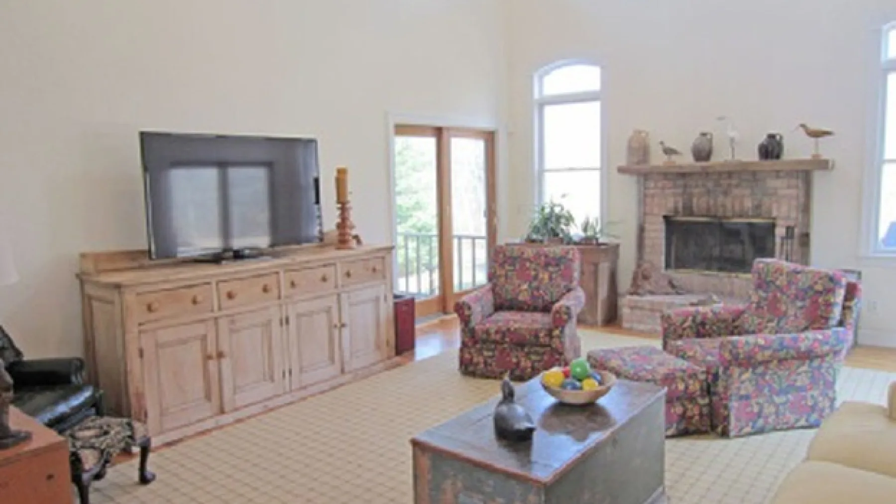 A bright living room with patterned seating, a television, and a stone fireplace.