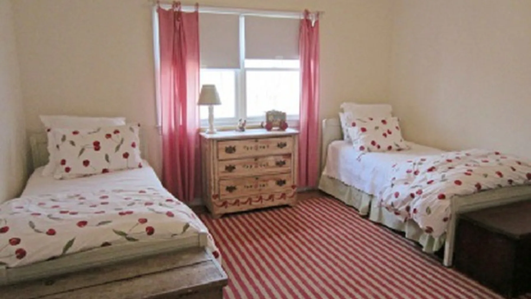 A bedroom with two beds, a dresser, and a striped rug.