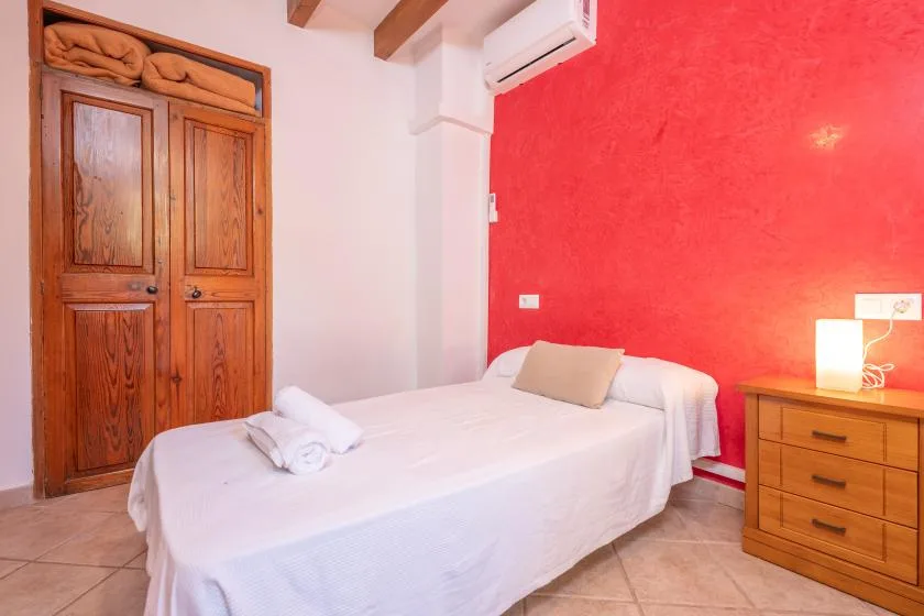 A bedroom with a bed beside a bright red wall and wooden dresser.
