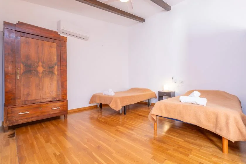 A bedroom with two beds covered in orange bedspreads and a wooden wardrobe.