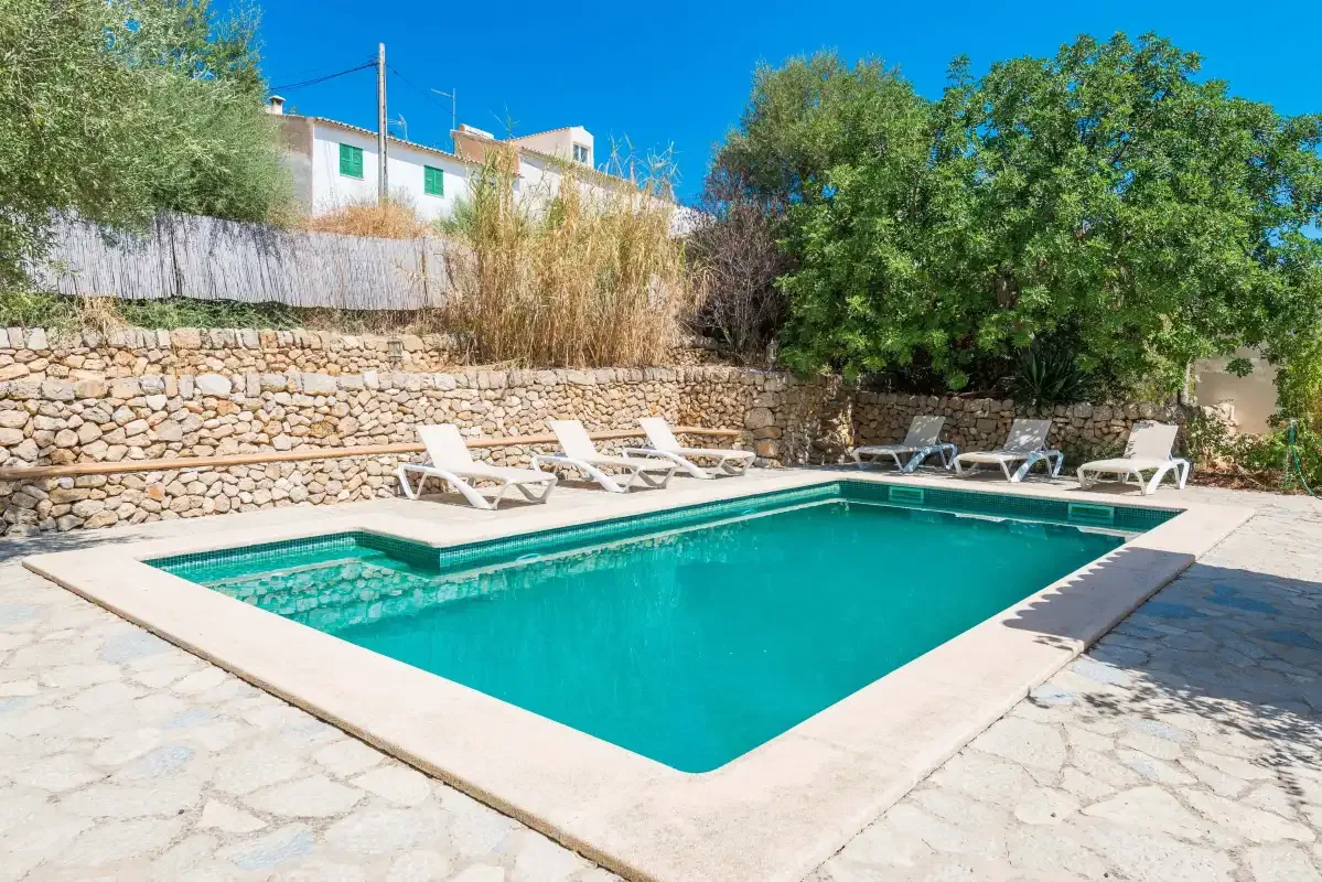 A swimming pool surrounded by a stone patio and sun loungers.