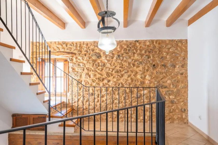 A staircase with black railings stands beside a textured stone wall beneath exposed ceiling beams.