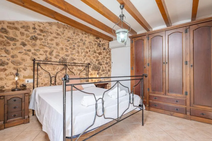 A bedroom with a metal bed, stone wall, and wooden wardrobe.