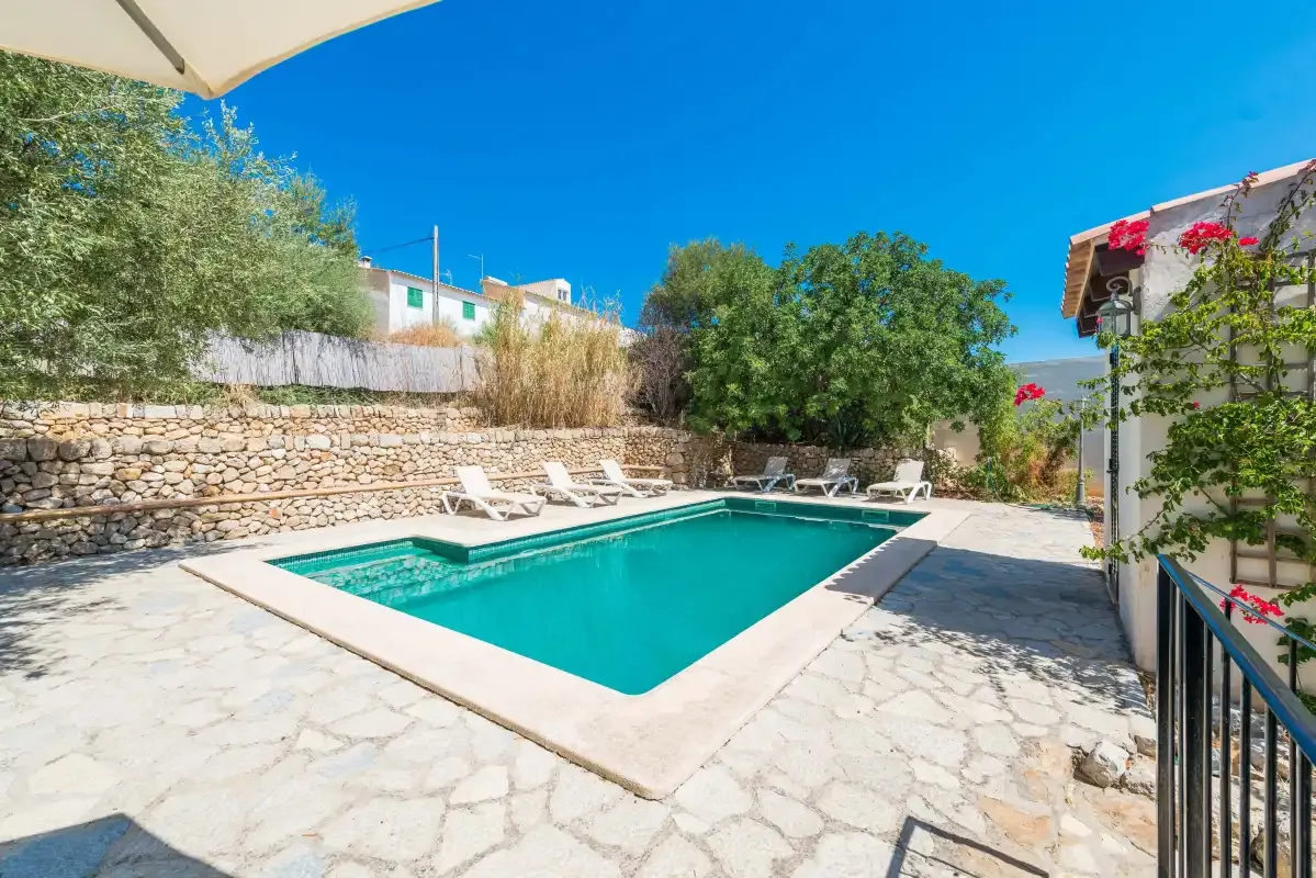 An outdoor swimming pool is surrounded by a paved patio and garden walls.