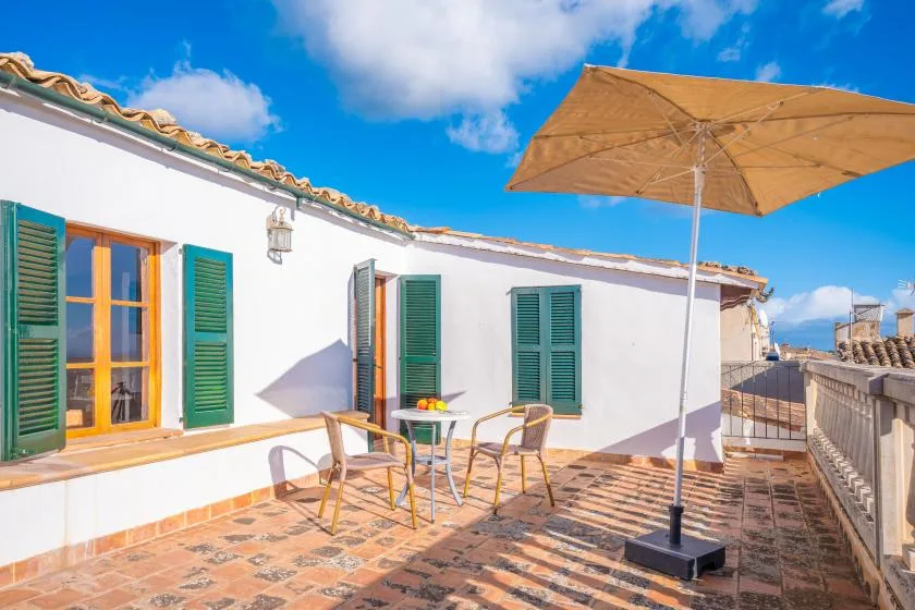 A sunny rooftop terrace with outdoor seating, green shutters, and a large umbrella.