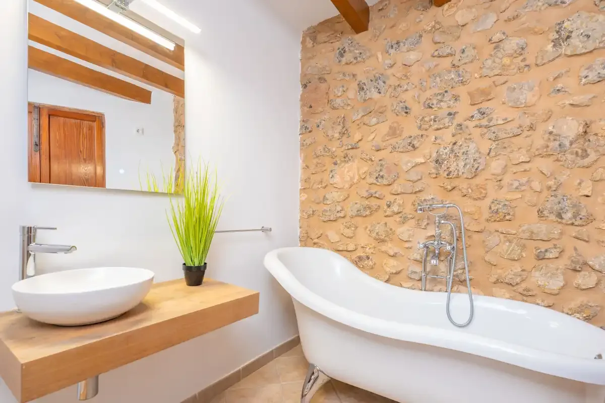 A bathroom with a freestanding bathtub beside a stone wall.