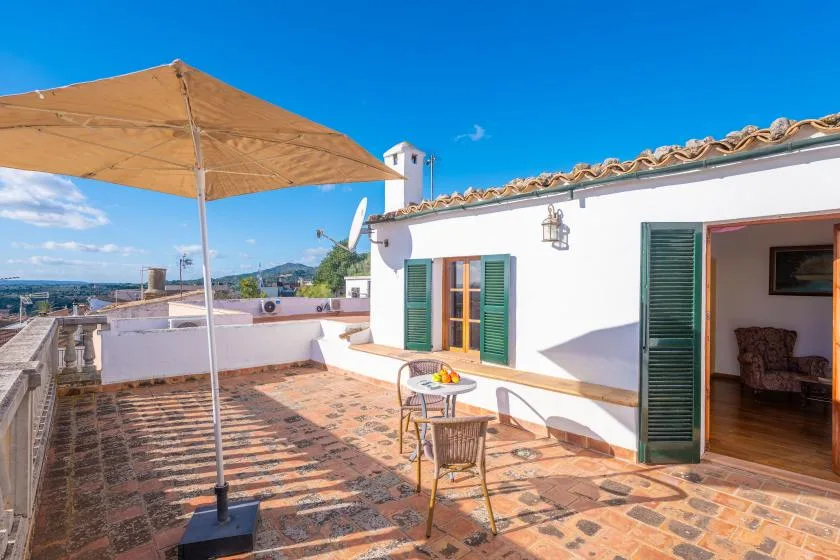A sunny tiled terrace beside a white building, with green shutters and an open doorway.