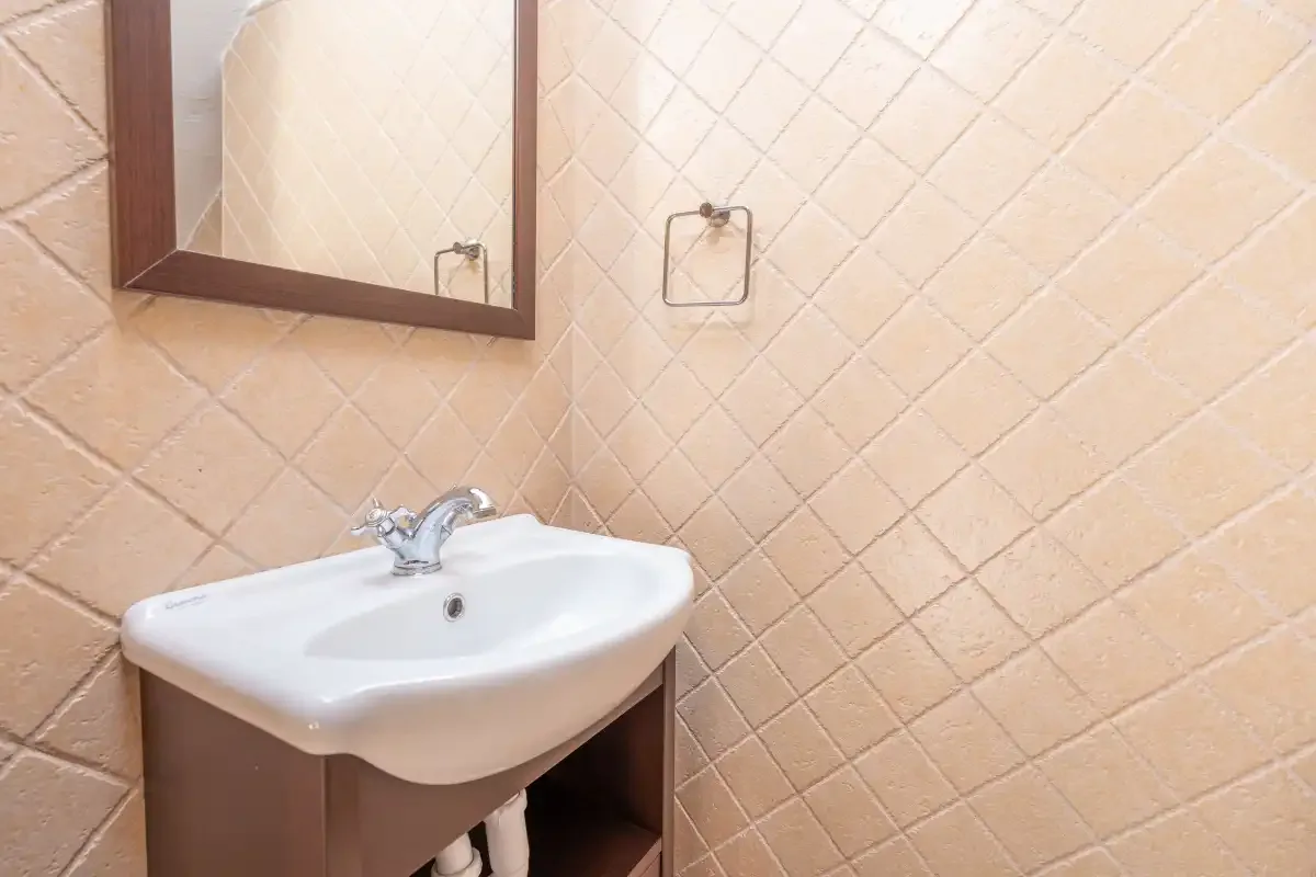 A bathroom sink sits beneath a wall mirror against tiled walls.