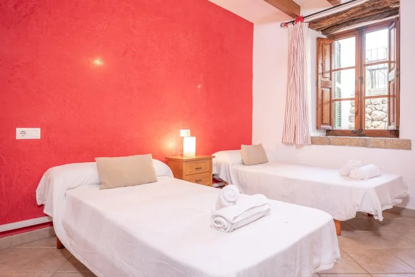 A bedroom with two beds, white linens, and a bright red wall.