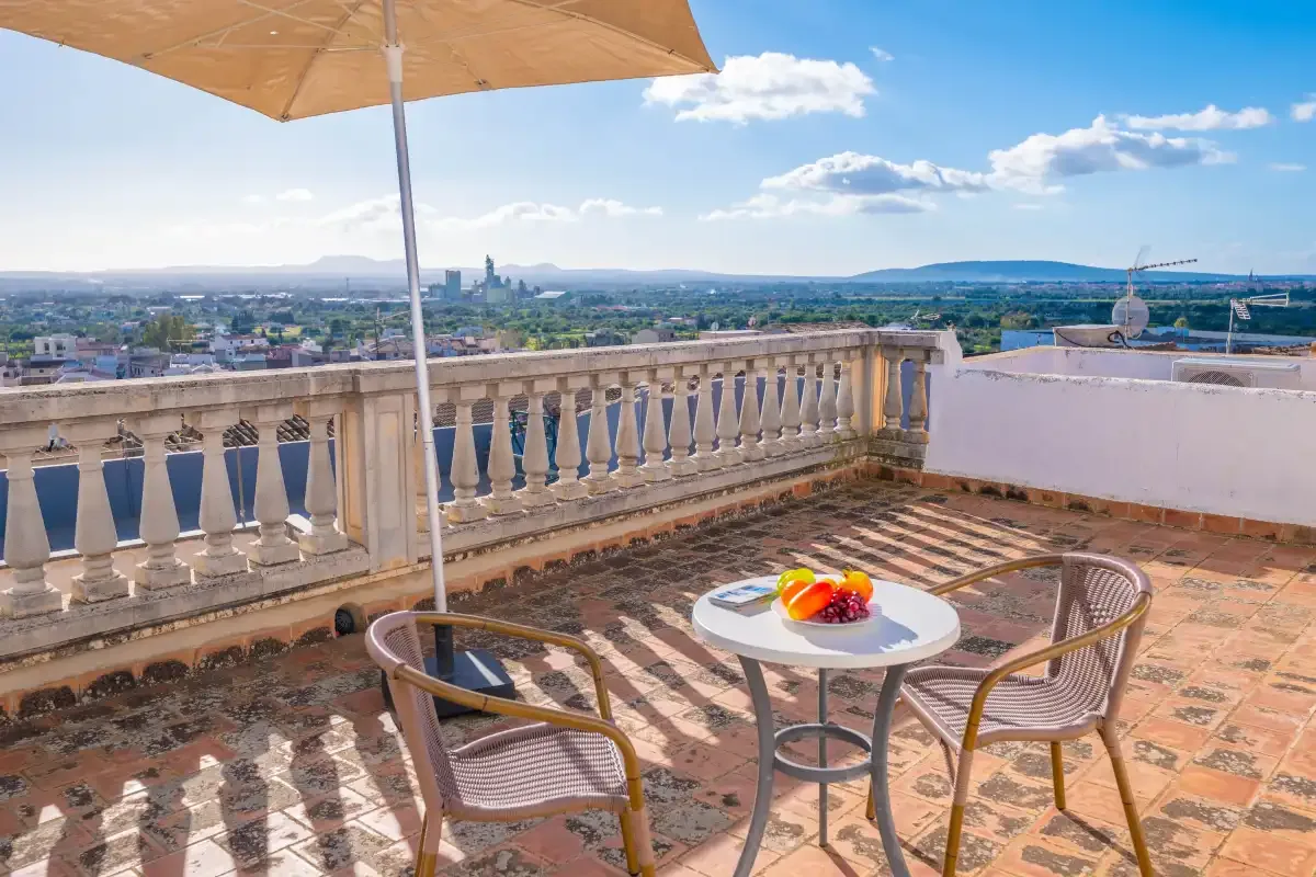 A rooftop terrace has a small table and seating beside a stone balustrade.