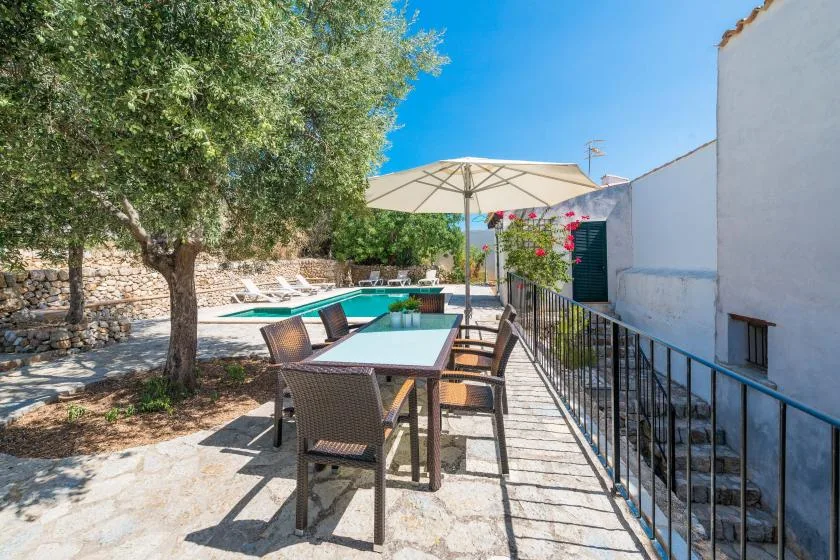 A stone patio with outdoor seating overlooks a swimming pool beneath a large umbrella.