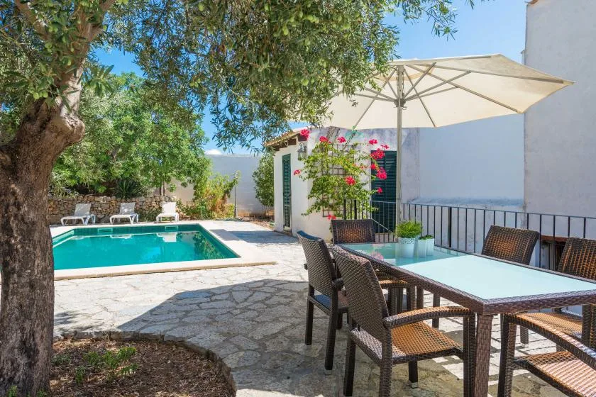 An outdoor pool and patio with seating beneath a large umbrella.