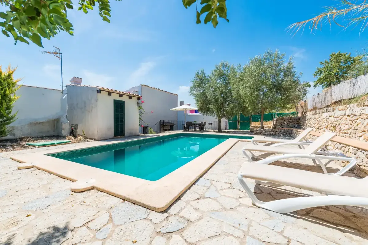 A swimming pool and loungers sit in a sunny outdoor courtyard.