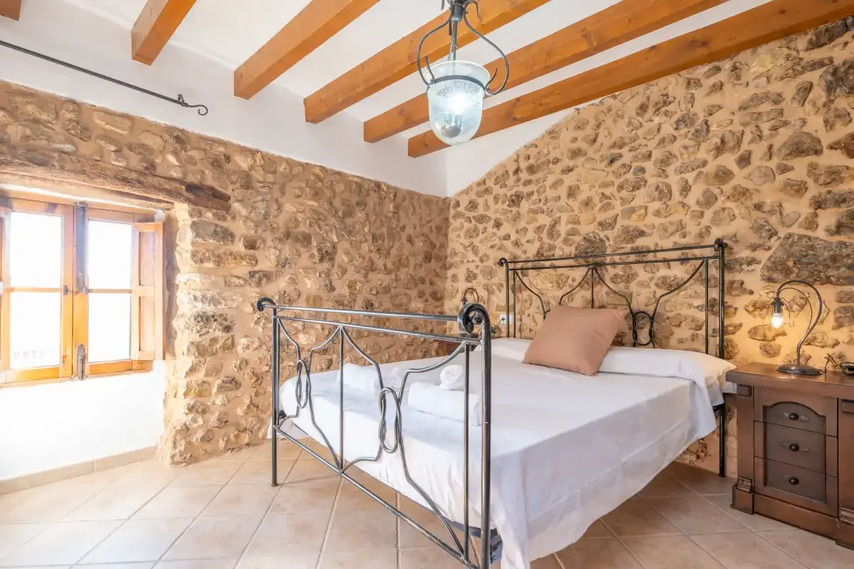 A bedroom with a metal bed, stone walls, and exposed wooden ceiling beams.