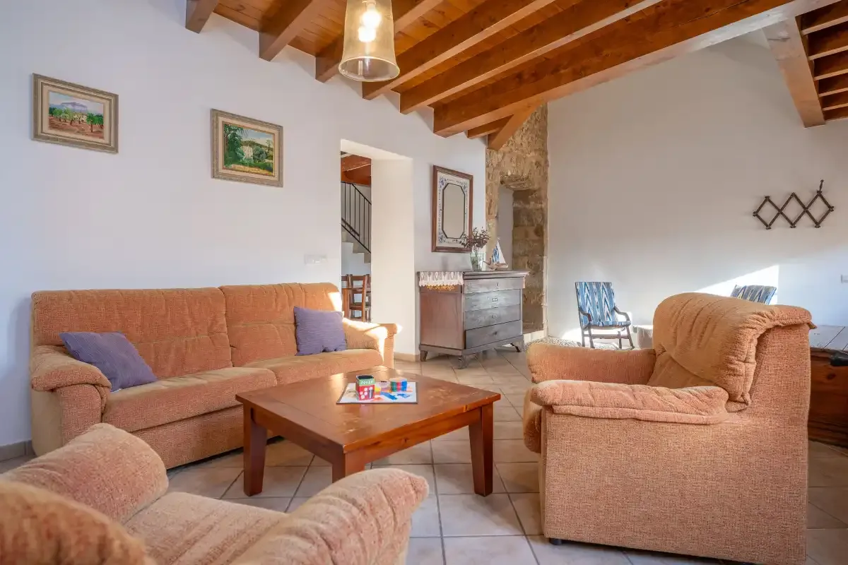 A living room with seating arranged around a wooden coffee table beneath exposed ceiling beams.