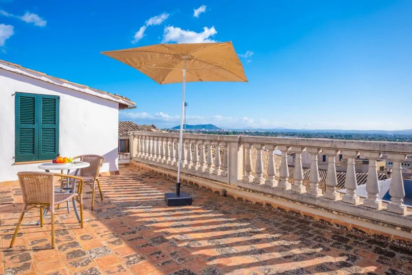 A sunlit terrace with a table, chairs, and a large patio umbrella.