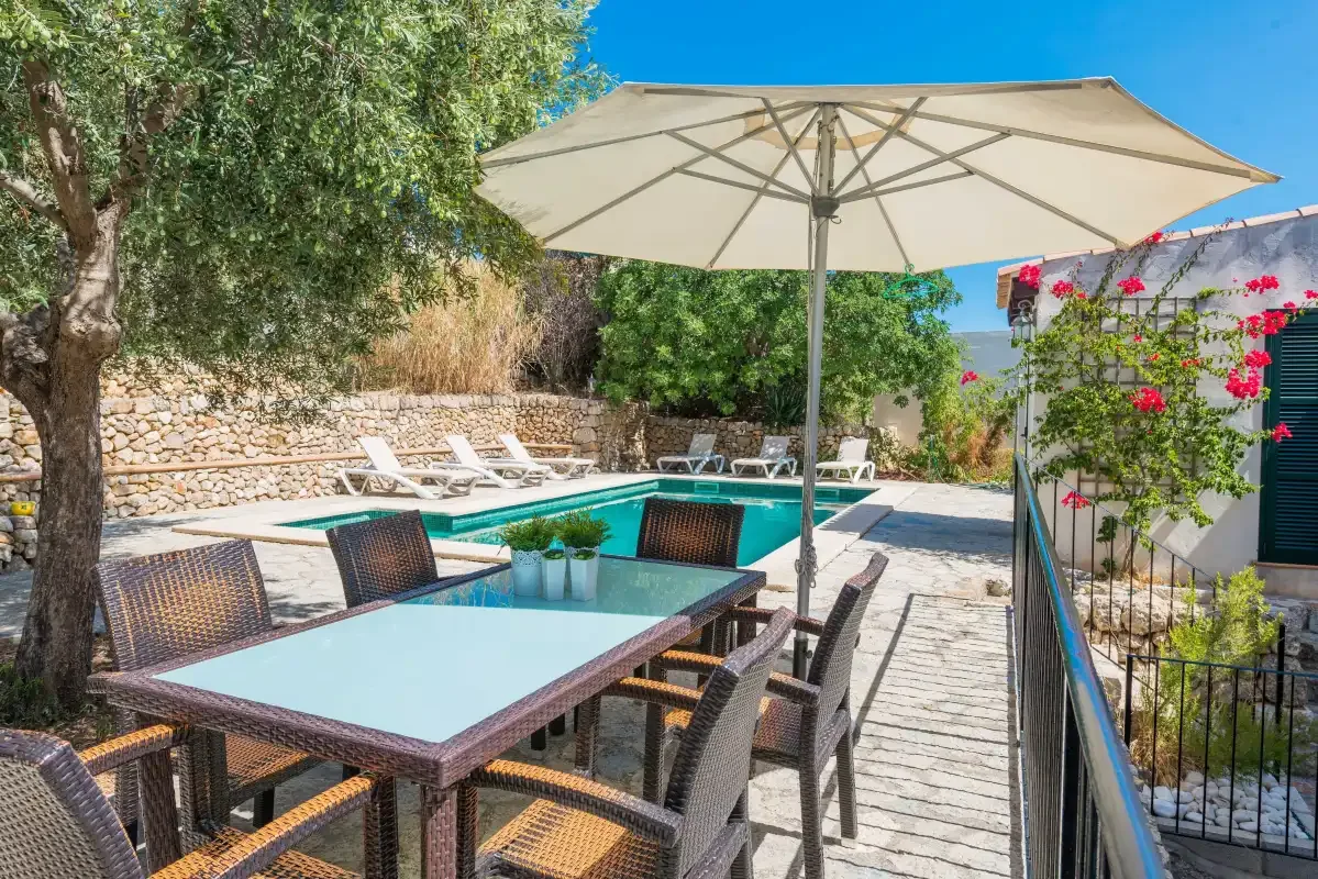 An outdoor dining area beside a swimming pool, with a large sun umbrella.