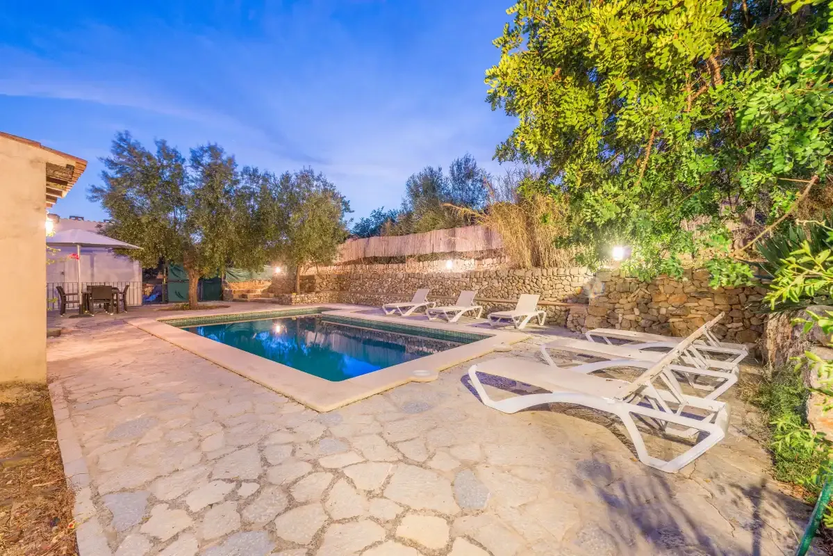 An outdoor swimming pool is surrounded by stone paving and lounge chairs.