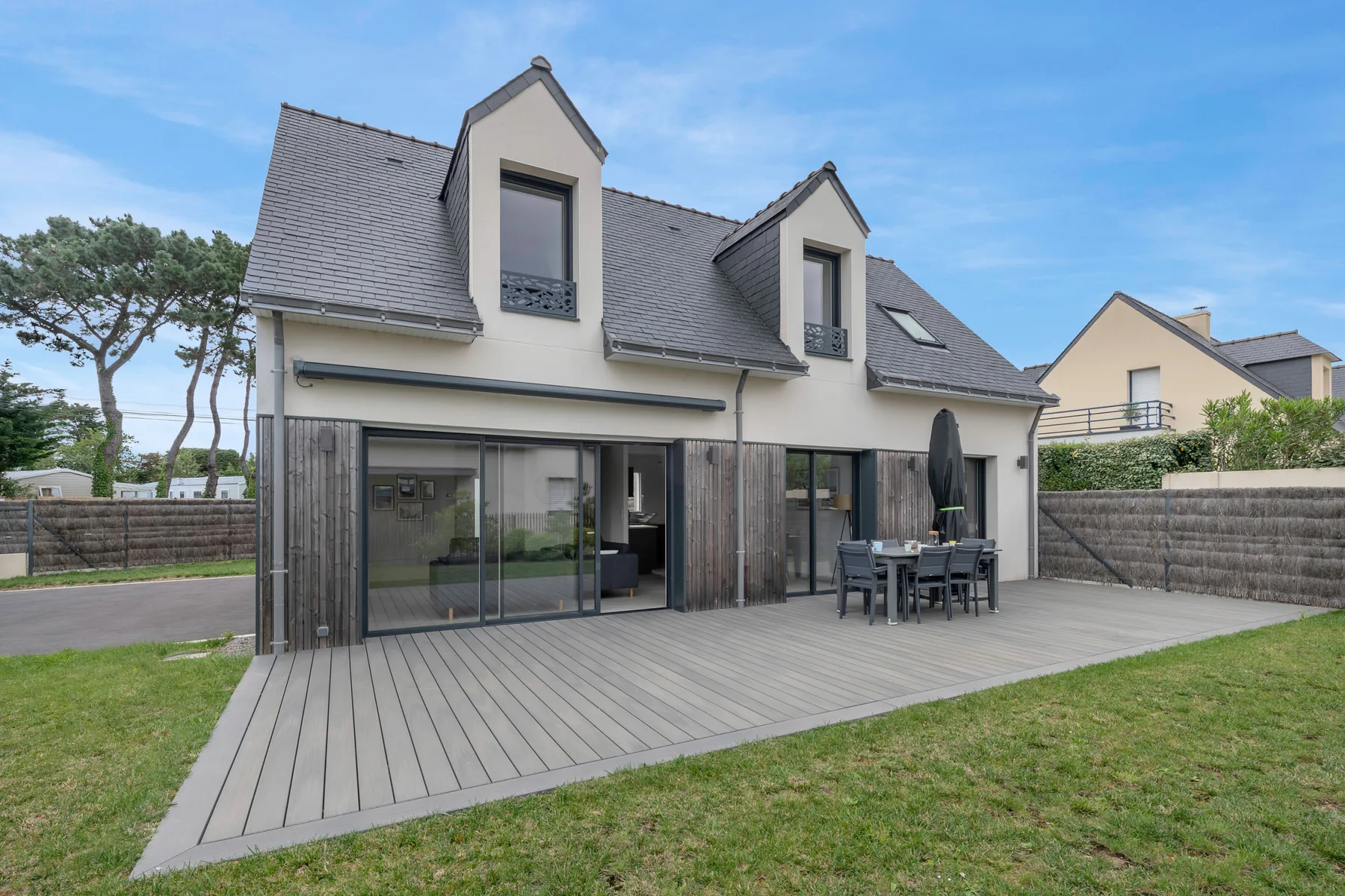 A modern house with a broad wooden deck and large glass doors.