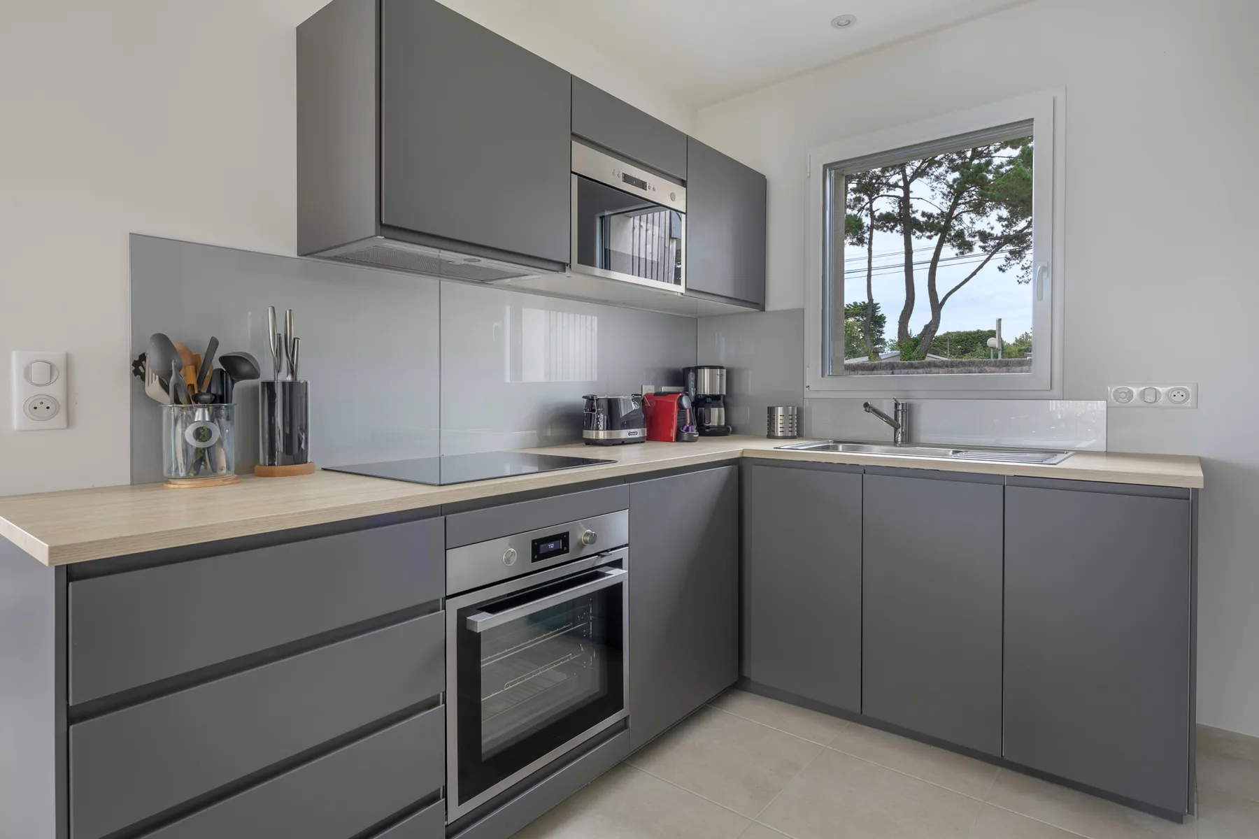 A modern kitchen with gray cabinetry, a built-in oven, and a window above the sink.