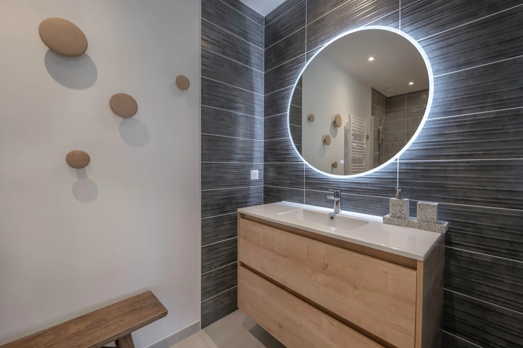 A bathroom vanity with a round illuminated mirror and wood cabinetry.