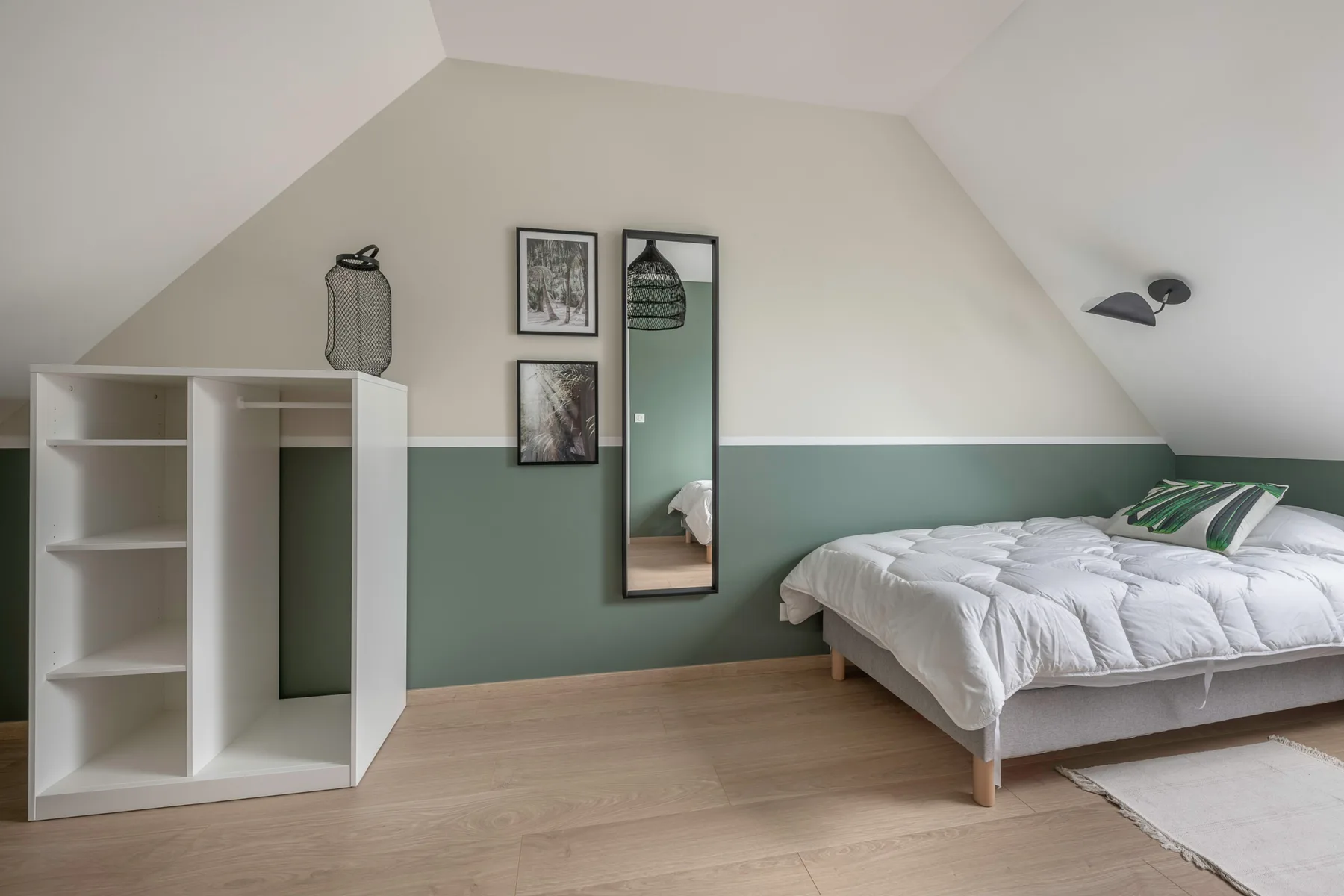 A bright attic bedroom with a bed, white shelving, and framed wall art.