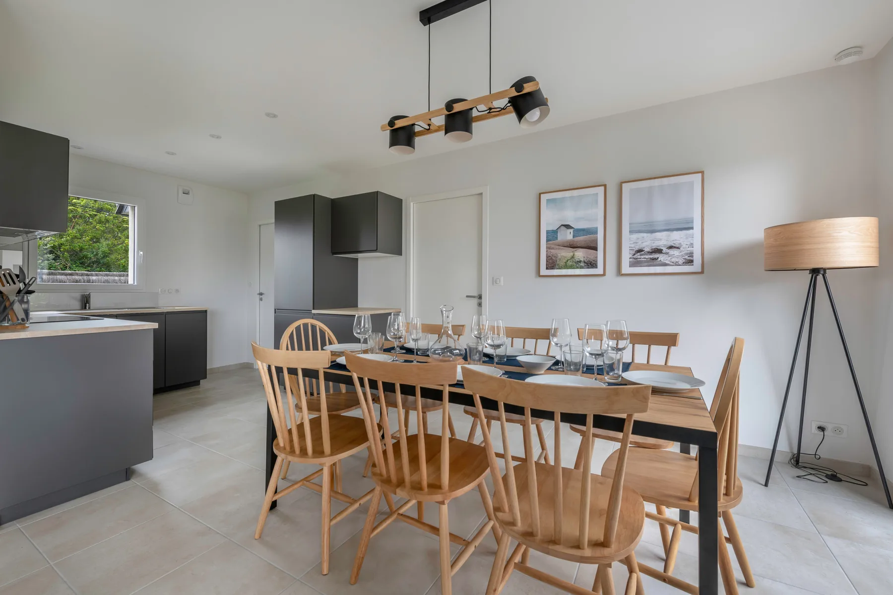 A dining area with a long wooden table and chairs beside an open kitchen.