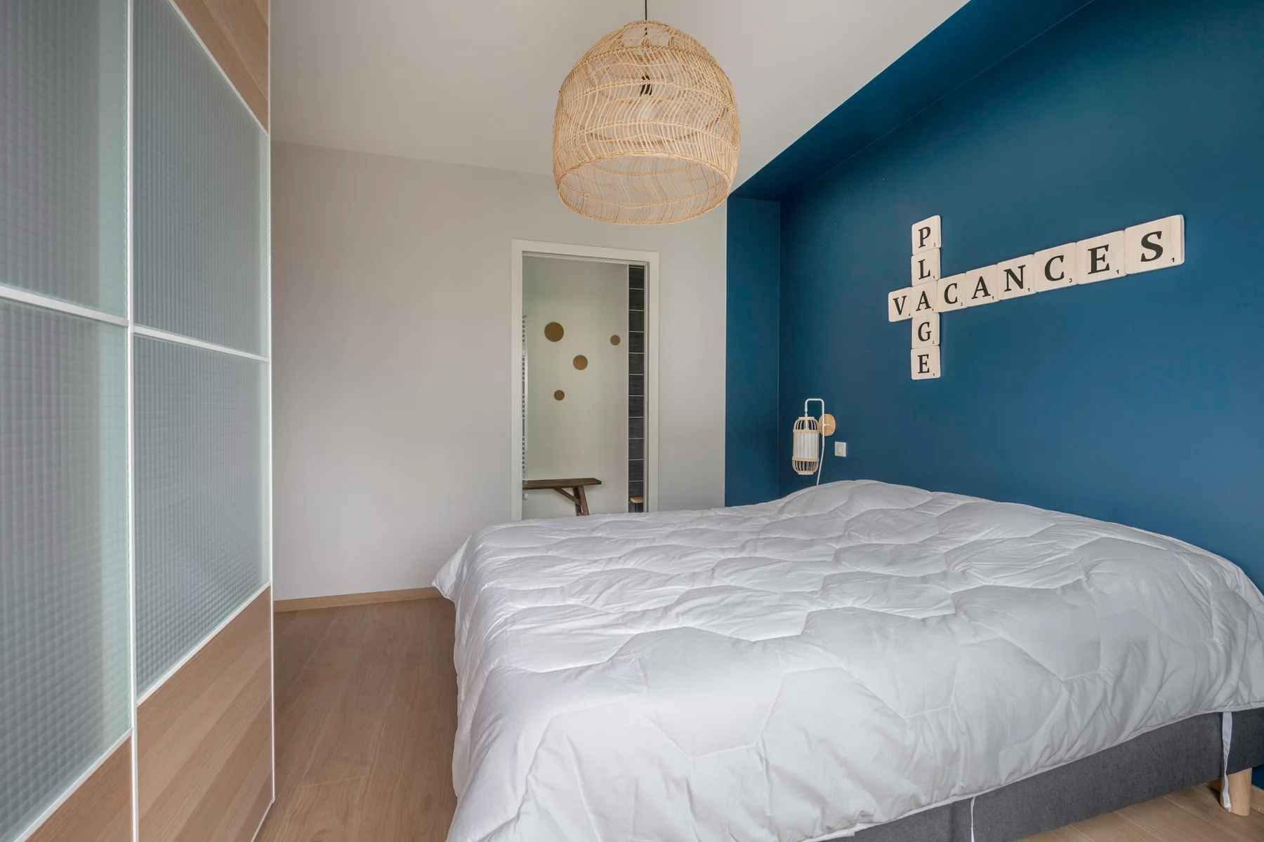 A bedroom with a bed, a blue accent wall, and a woven pendant light.
