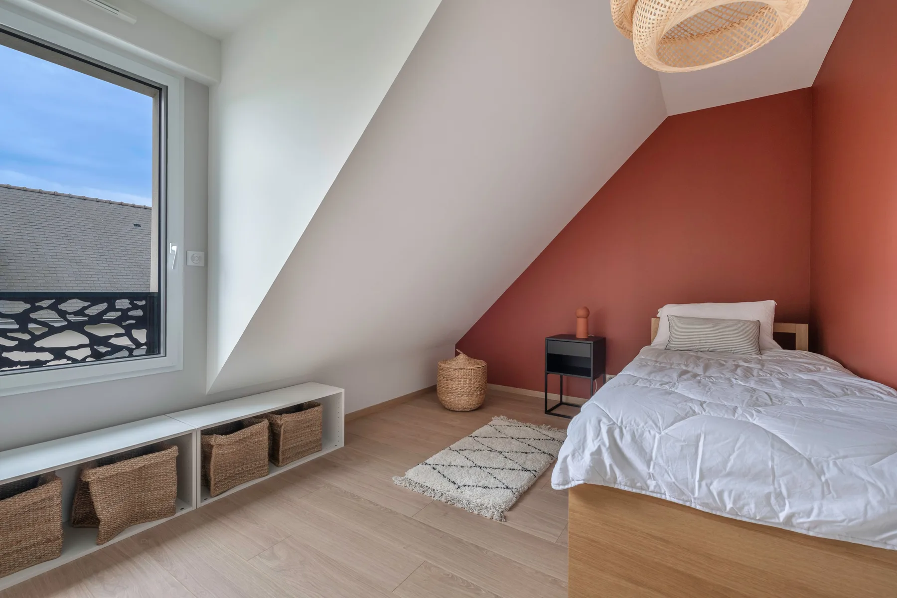 A bedroom with a bed beneath a sloped ceiling and a large window.