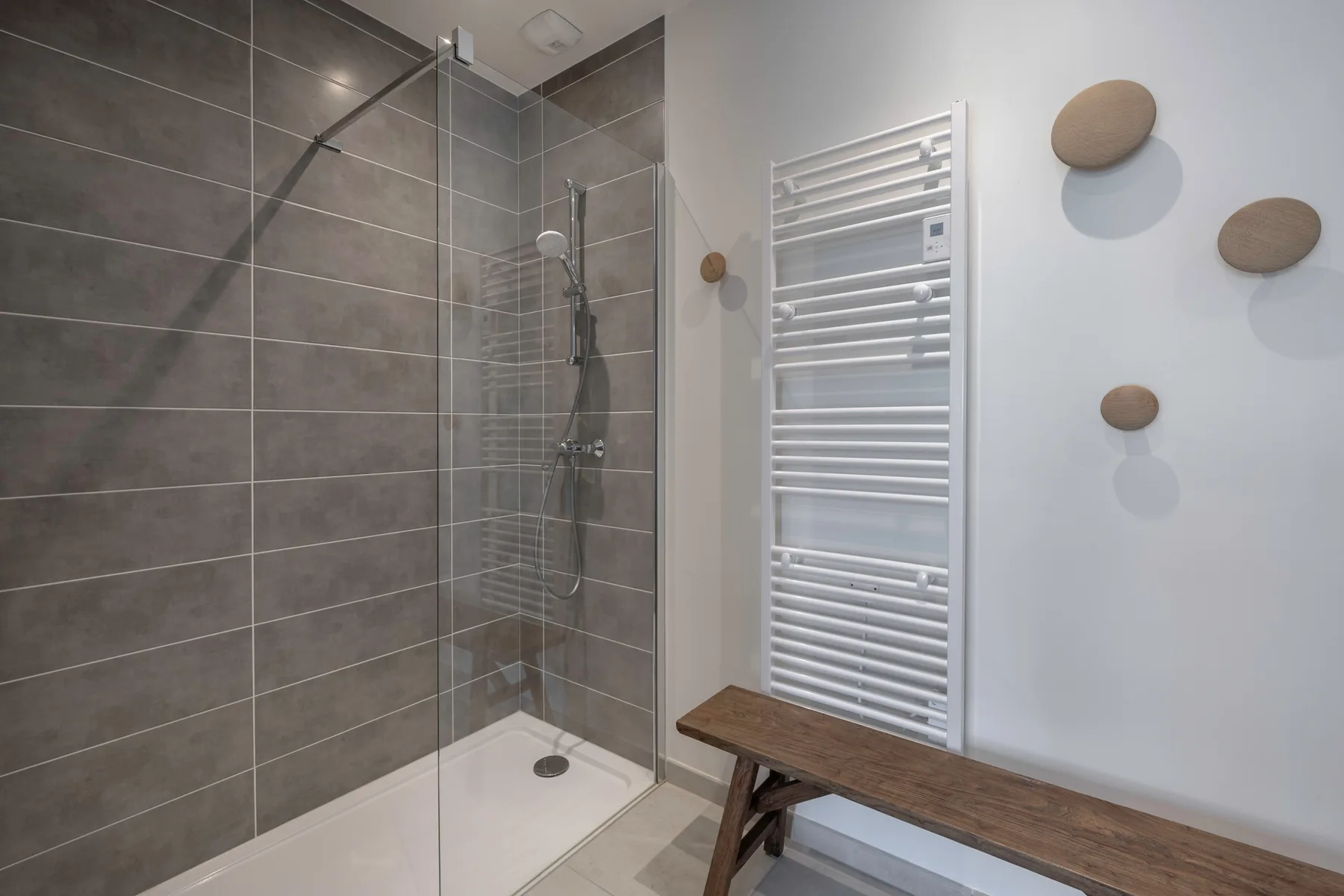 A tiled bathroom shower area with a white towel radiator and wooden bench.