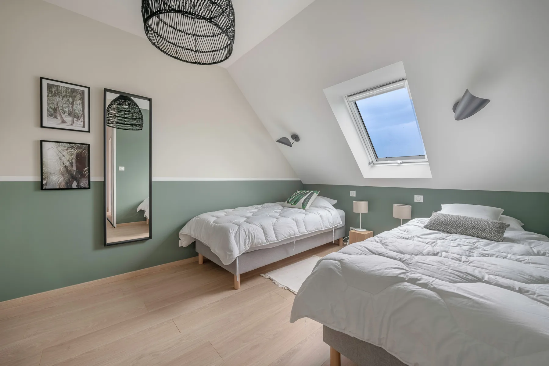 A bright bedroom with two beds, framed prints, and a skylight.