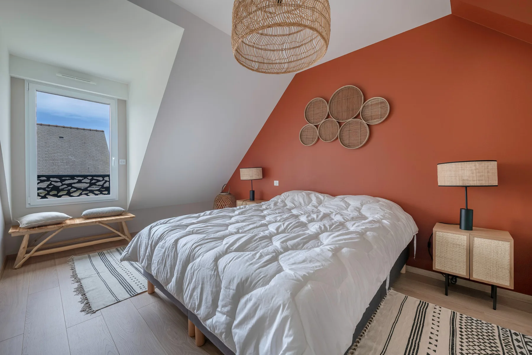 A bedroom with a bed, an orange accent wall, and a window.