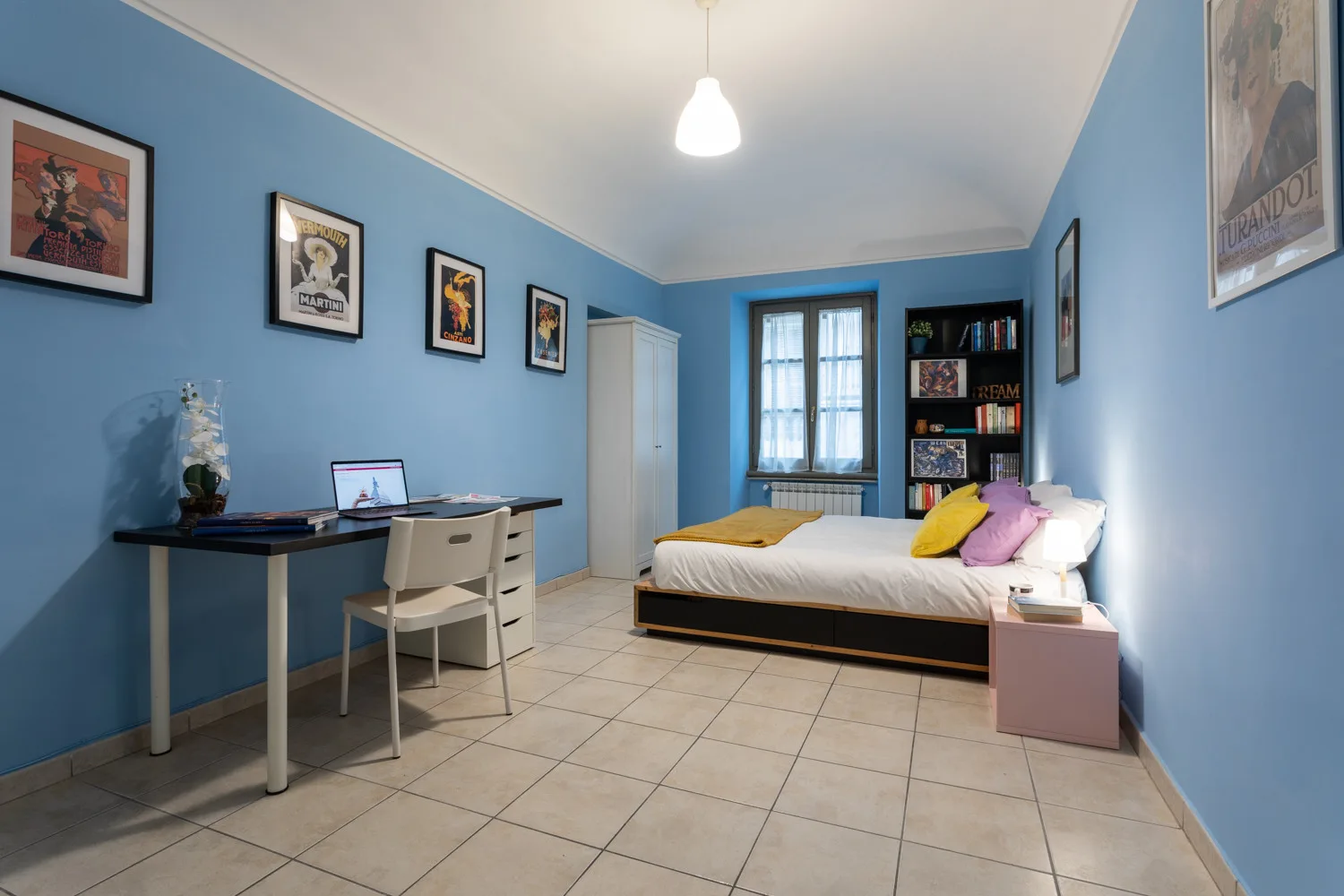 Un dormitorio con cama, escritorio y cuadros en paredes azules.