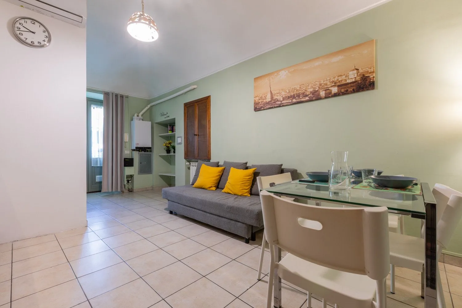 Una sala de estar y comedor con un sofá gris y una mesa de comedor de vidrio.