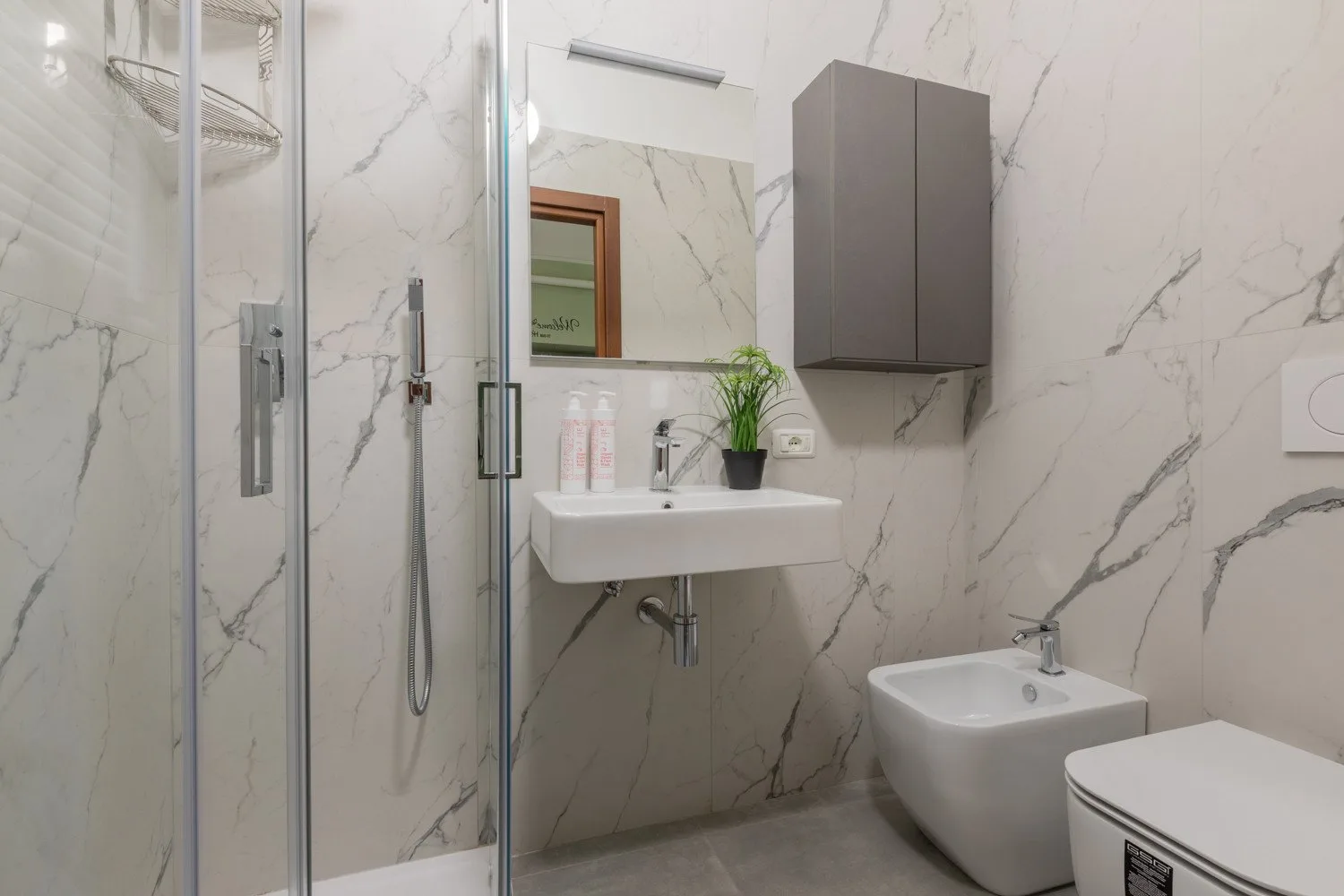 Un baño moderno con ducha de vidrio, lavabo suspendido e inodoro.