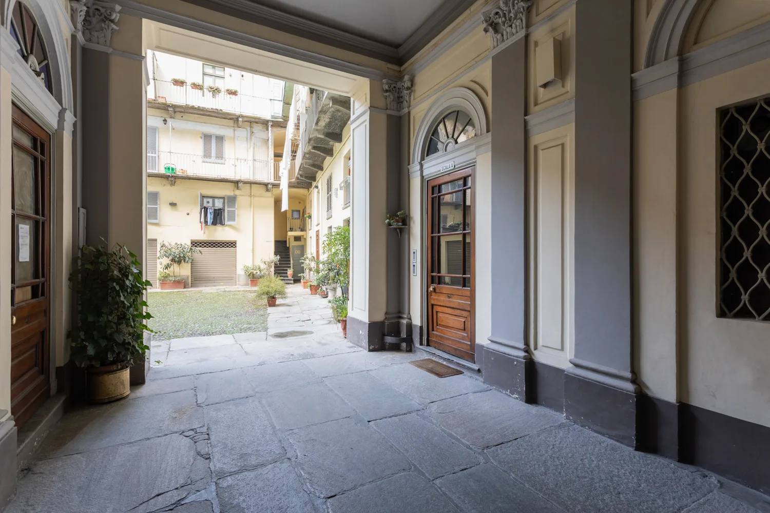 Un pasaje de entrada cubierto se abre a un patio pavimentado con plantas en macetas.