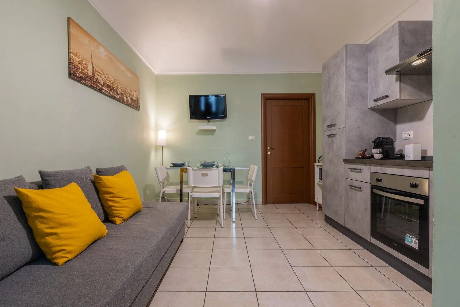 Una pequeña zona de estar y cocina con sofá gris y mesa de comedor.