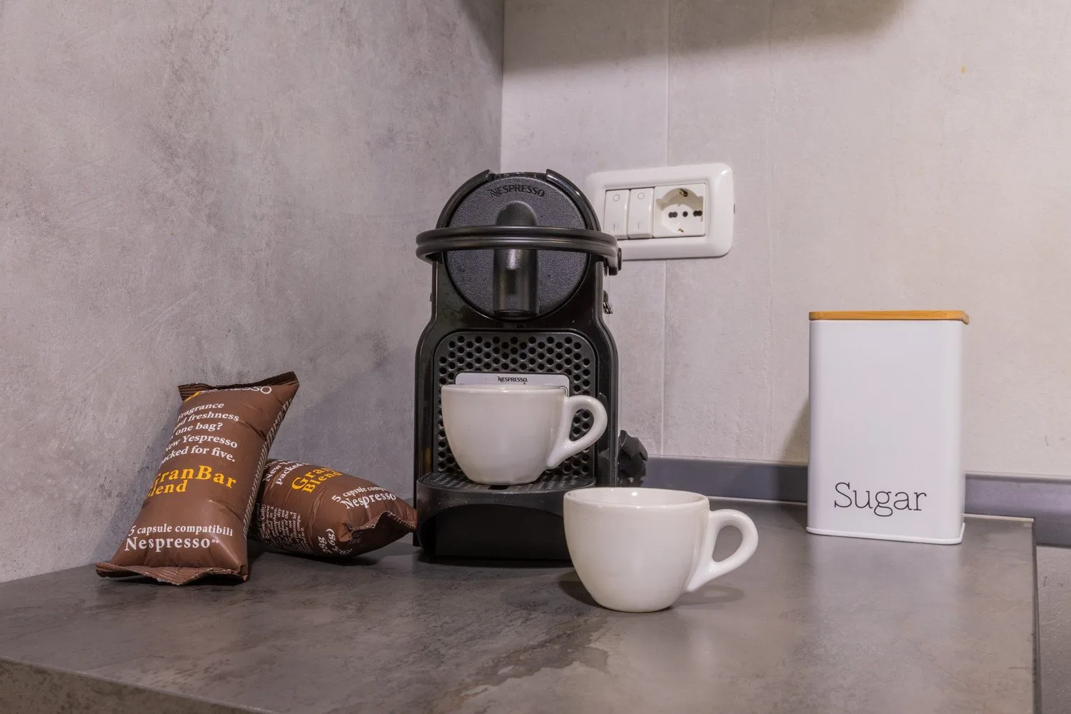 Una cafetera y tazas están sobre una encimera junto a un recipiente de azúcar.