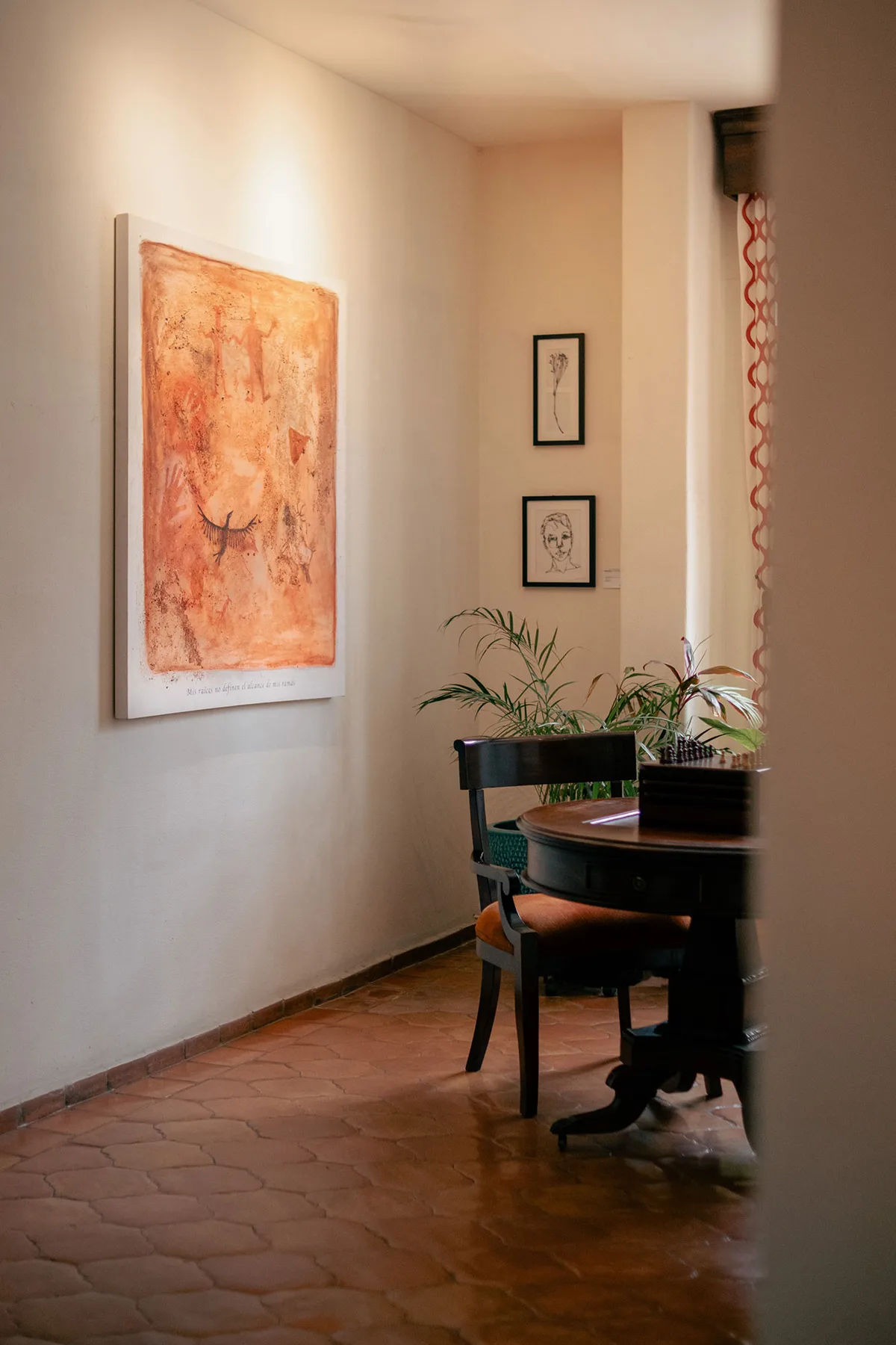 Área de estar del hotel con una mesa redonda, una silla, plantas y obras de arte.