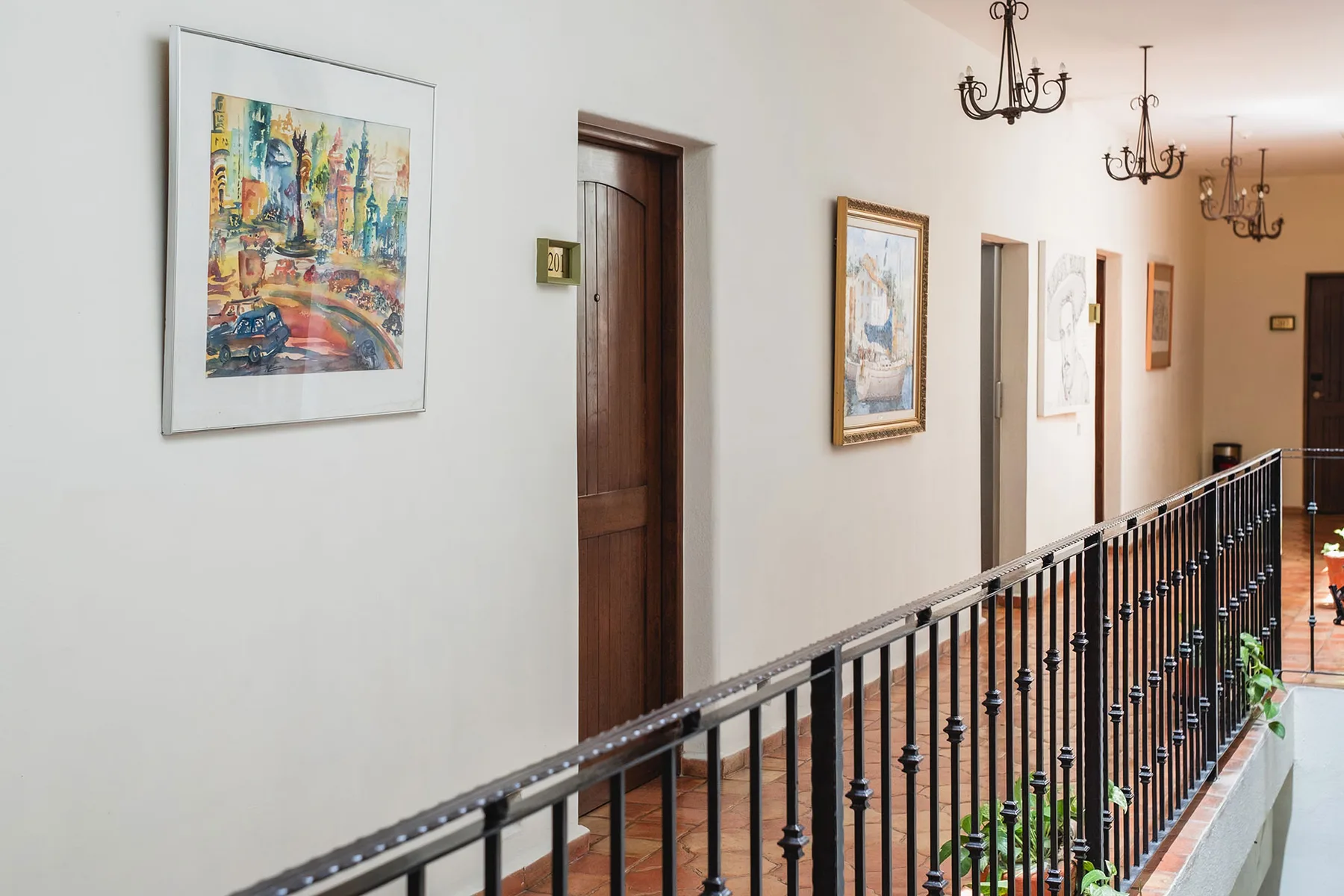 Pasillo del hotel con obras de arte, plantas y una puerta de madera de una habitación.