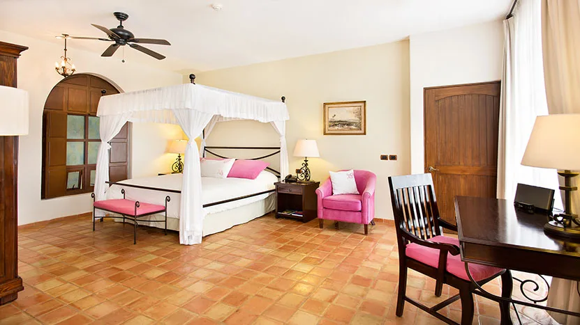 Habitación con cama con dosel, sillas, escritorio y piso de loseta de terracota.