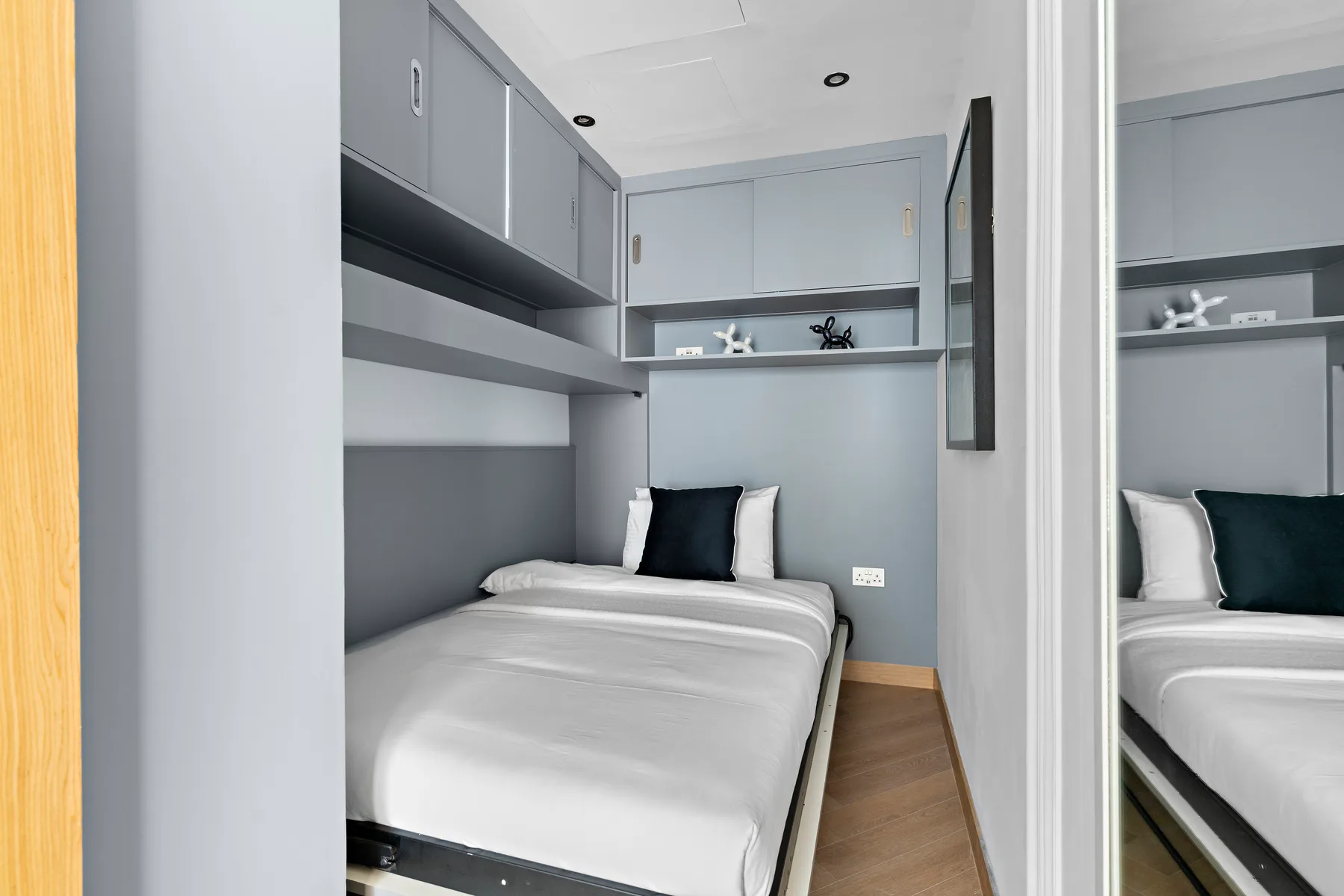 Un dormitorio compacto con una cama bien tendida y armarios empotrados grises.