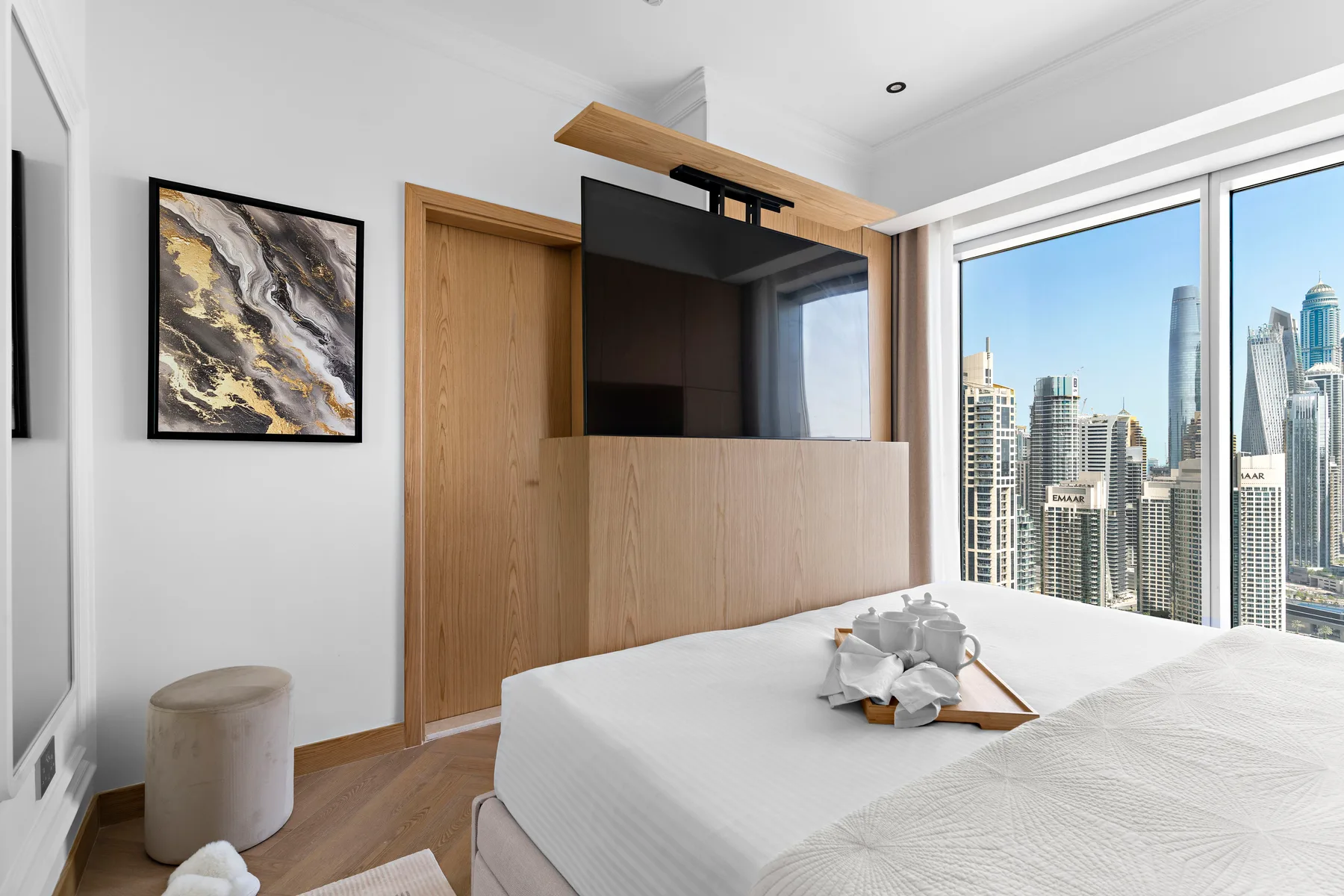Un dormitorio luminoso con una cama, una pared de madera con televisor y vistas a la ciudad.