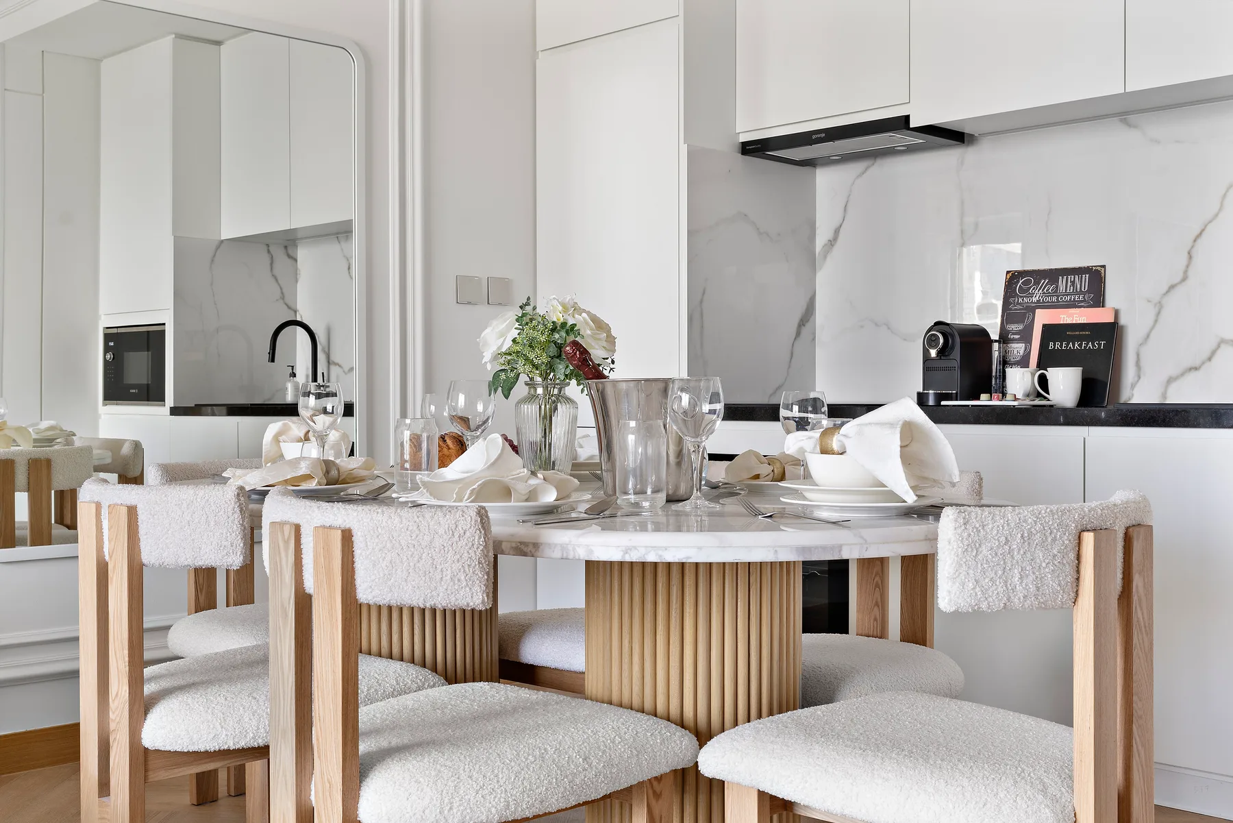 Comedor con la mesa puesta y asientos tapizados junto a una cocina moderna.