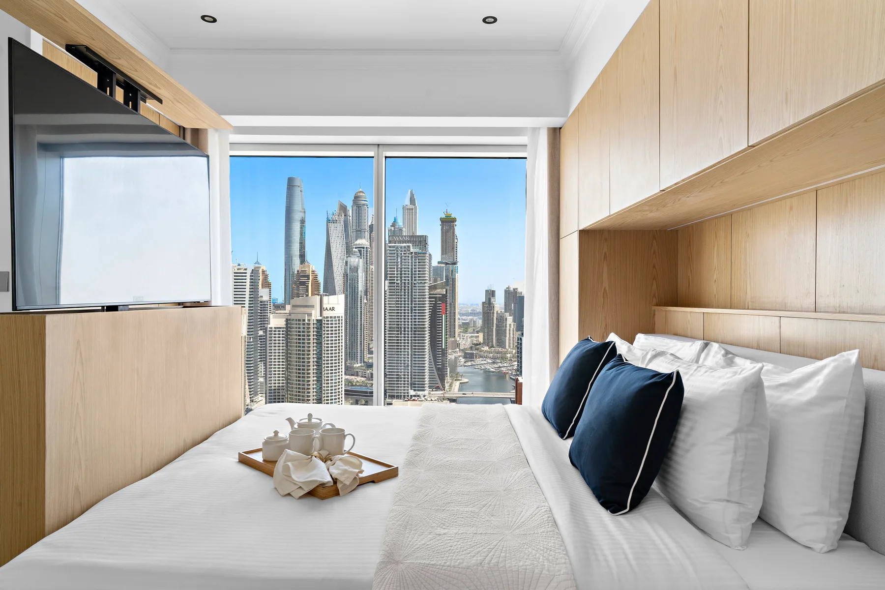 Un dormitorio con la cama ordenada y el perfil urbano visible por la ventana.