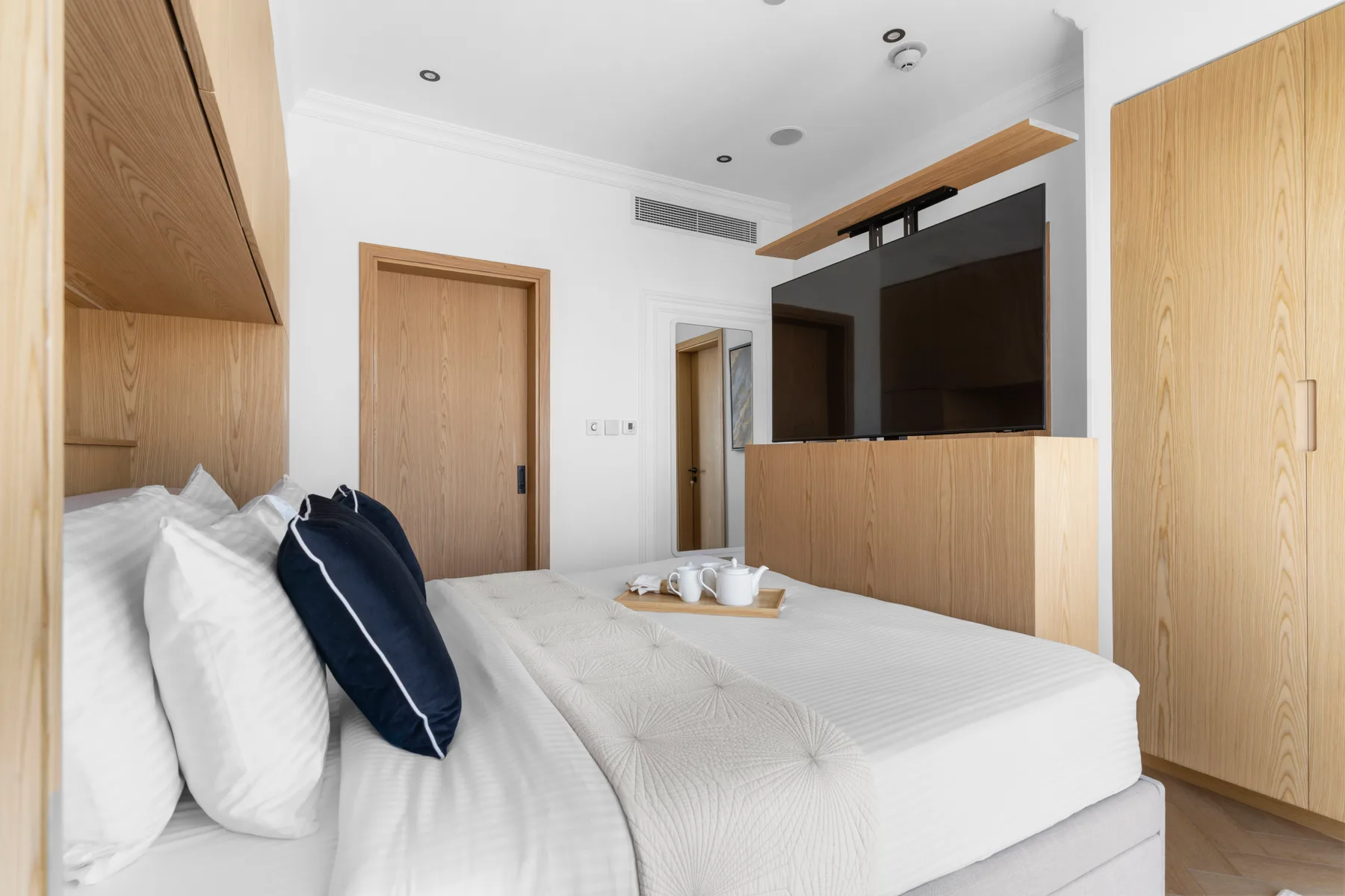Un dormitorio luminoso con una cama y un televisor integrado en una pared revestida de madera.