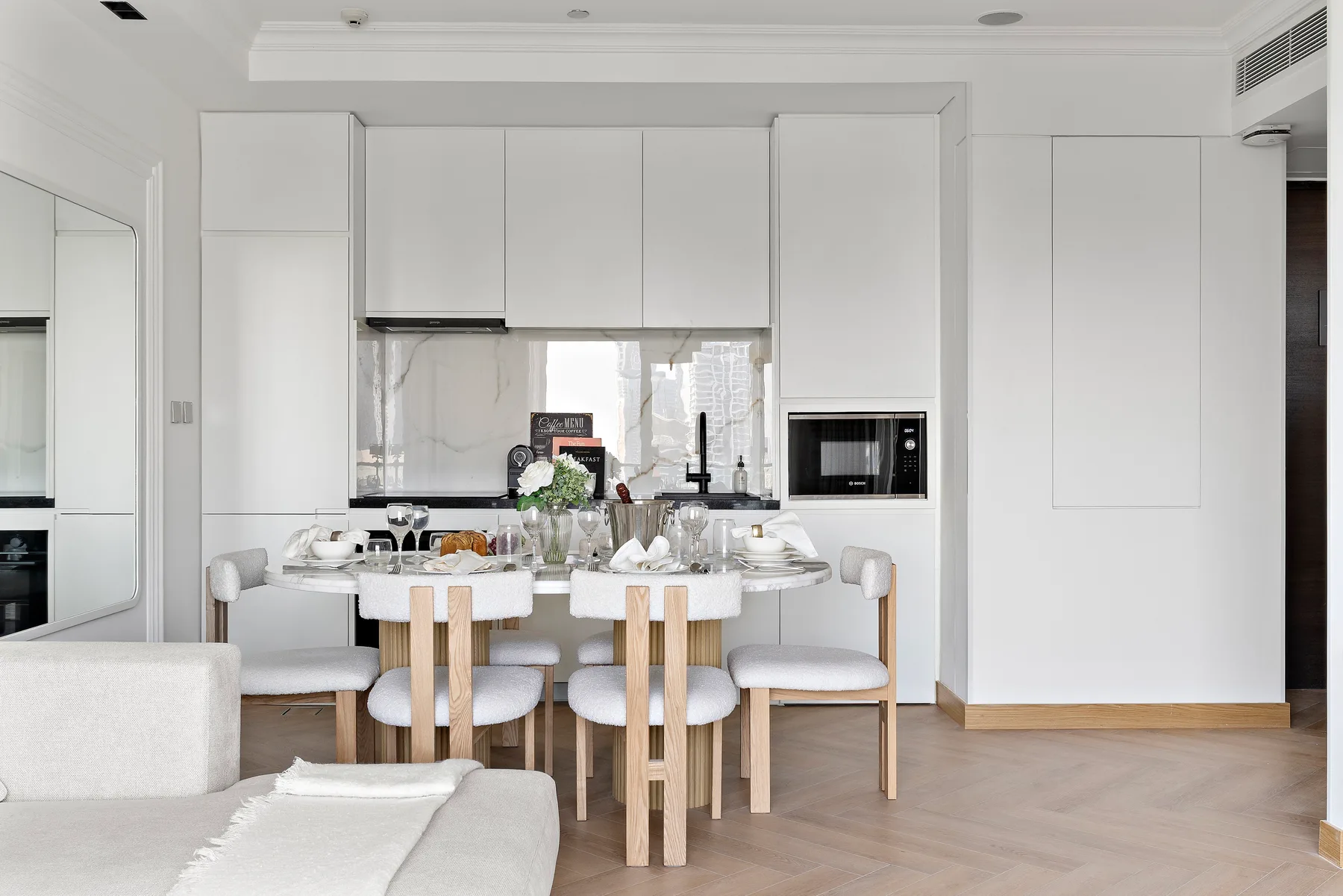 Un comedor luminoso con una mesa puesta frente a armarios blancos de cocina.